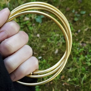 May include: A set of four gold metal rings, interlocked and held in a hand. The rings are smooth and shiny.