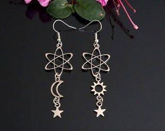 May include: Silver-toned celestial earrings. Each earring features a star-shaped design with a dangling crescent moon and star on one, and a sun and star on the other. The earrings are displayed against a black background.