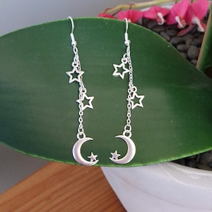 May include: Silver dangle earrings with a crescent moon charm and multiple star charms hanging from a silver chain.