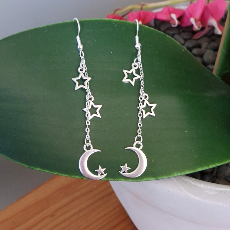 May include: Silver dangle earrings with a crescent moon charm and multiple star charms hanging from a silver chain.