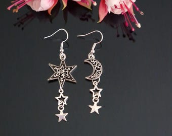 May include: Silver dangle earrings with a star and moon design. The star has a filigree pattern and is accented with two smaller stars. The moon is crescent shaped and also has a filigree pattern.
