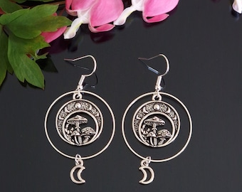 May include: Silver hoop earrings with a crescent moon charm dangling from the bottom. The hoop features a detailed design of mushrooms and a crescent moon.