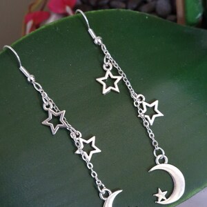 May include: Silver dangle earrings with a crescent moon charm and multiple star charms hanging from a chain.