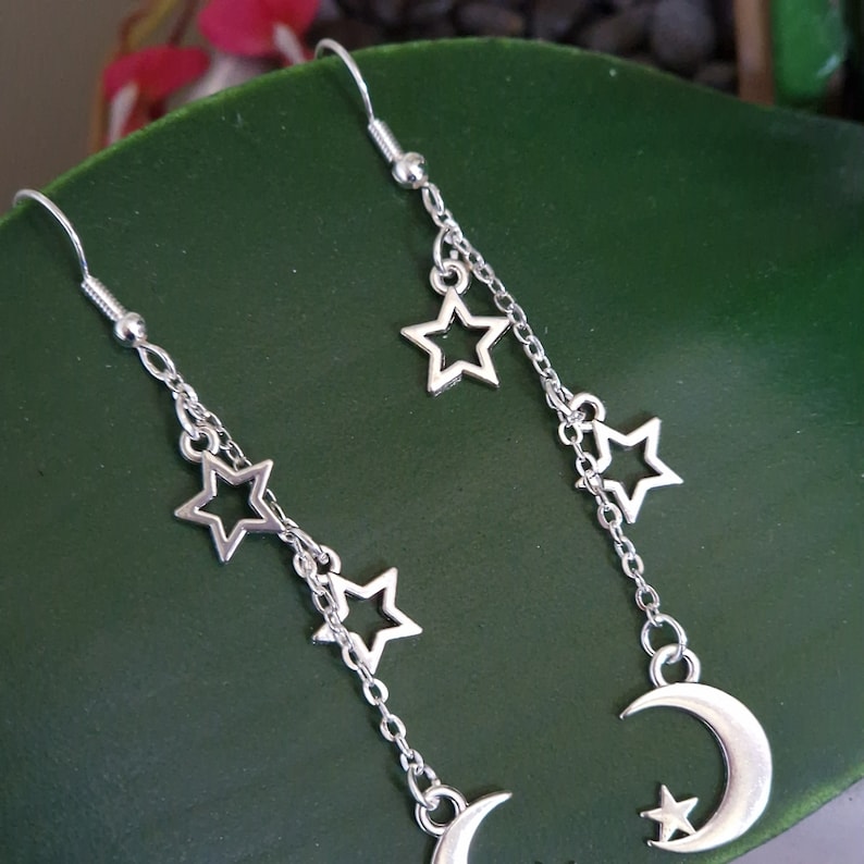 May include: Silver dangle earrings with a crescent moon charm and multiple star charms hanging from a chain.
