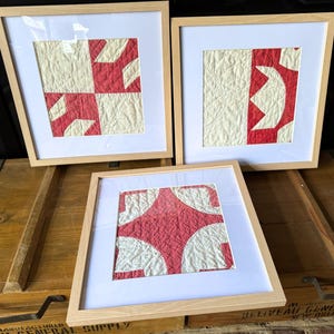 May include: Three framed red and white patchwork quilt squares in wooden frames. The frames are light brown wood.