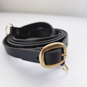 May include: A black leather camera strap with a gold metal buckle and two gold metal rings.