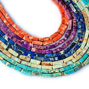 May include: A close-up of a multi-colored gemstone bead strand. The beads are rectangular and have a marbled pattern. The colors of the beads are turquoise, blue, purple, orange, and red.