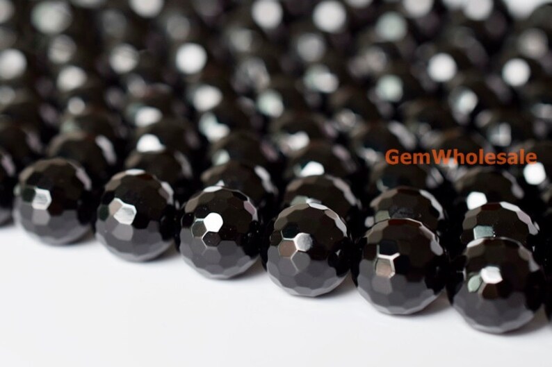 May include: Close-up of a collection of faceted black beads. The beads have a glossy, reflective surface and a geometric pattern. The beads are likely used for jewelry making or crafting.