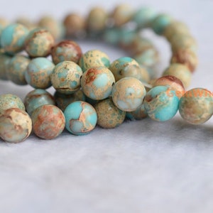 May include: A strand of round, blue, brown, and white marbled gemstone beads. The beads are strung on a clear elastic cord.