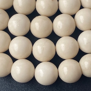 Puede incluir: Primer plano de una colección de cuentas redondas blancas. Las cuentas son lisas y tienen un ligero brillo.