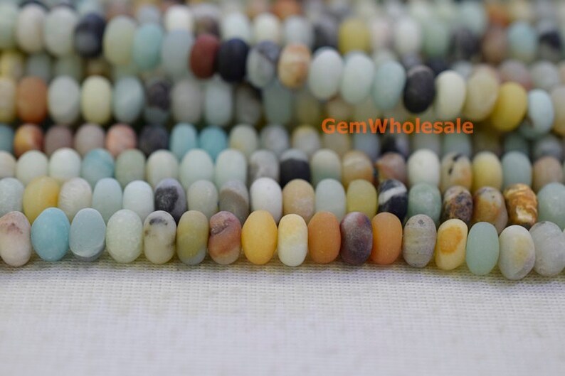 May include: Close-up of a strand of oval-shaped gemstone beads in various colors, including blue, yellow, brown, and white. The beads are strung together, creating a textured and colorful pattern. The beads are approximately 0.8 cm in length.