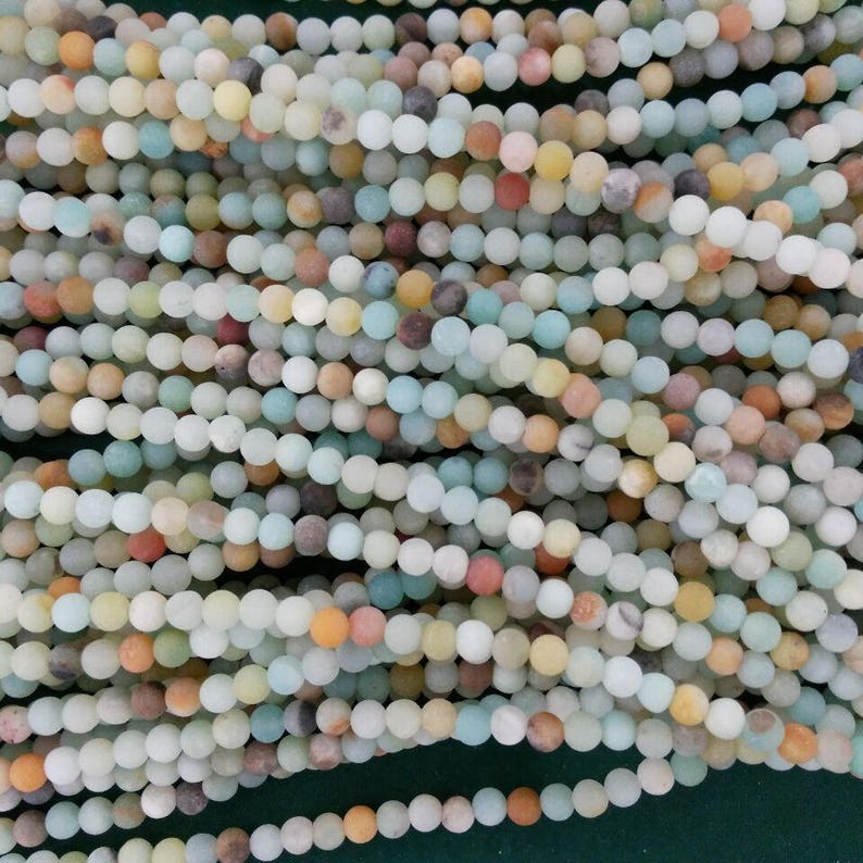 May include: A strand of multi-colored round beads made of natural stone. The beads are a mix of green, blue, brown, yellow, and orange.