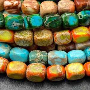 May include: Close-up of a collection of colorful, polished gemstone beads. The beads are square-shaped and feature a variety of colors, including turquoise, green, orange, yellow, and brown. The beads are arranged in rows, creating a visually appealing pattern.