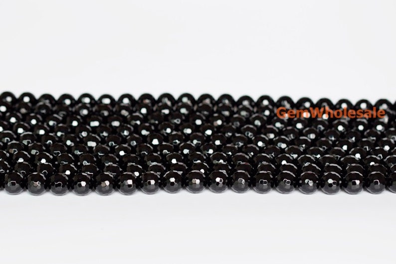 May include: Strands of faceted black beads, likely onyx or a similar gemstone, are displayed against a white background. The beads are round and have a polished, reflective surface. The image showcases the beads' color and texture.