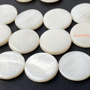 May include: A close-up of a collection of white round mother of pearl beads. The beads have a smooth, polished surface and a subtle iridescent sheen.