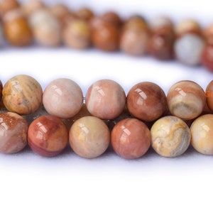 May include: A strand of round, brown, beige, and pink gemstone beads. The beads have a marbled pattern and a smooth, polished finish.