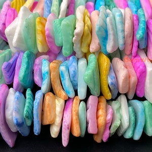 May include: A strand of colorful, irregular shaped, flat, gemstone beads. The beads are in shades of blue, green, pink, yellow, and white.