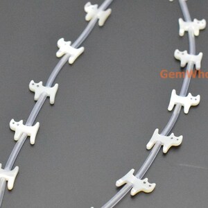 May include: A strand of white mother of pearl cat beads strung on a clear elastic cord. The beads are approximately 1/2 inch in size and feature a simple cat design.