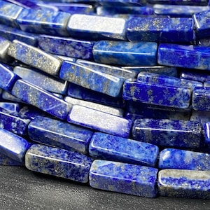 Peut inclure: Gros plan sur un brin de perles de lapis-lazuli bleu foncé. Les perles sont rectangulaires et ont une finition polie. Le lapis-lazuli a un aspect moucheté caractéristique avec des inclusions de pyrite dorée.