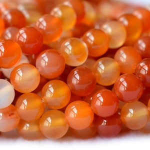May include: A strand of round, orange carnelian beads. The beads are smooth and polished, with a translucent appearance.