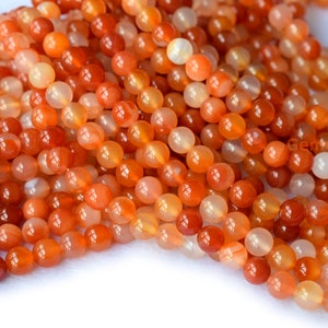 May include: A strand of smooth, round, orange carnelian beads. The beads are translucent and have a slight shimmer.