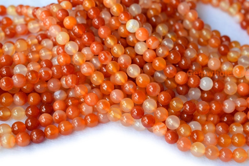 May include: A strand of smooth, round, orange carnelian beads. The beads are translucent and have a slight shimmer.