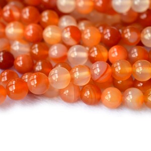 May include: A strand of orange carnelian beads. The beads are round and smooth, with a translucent, agate-like appearance.