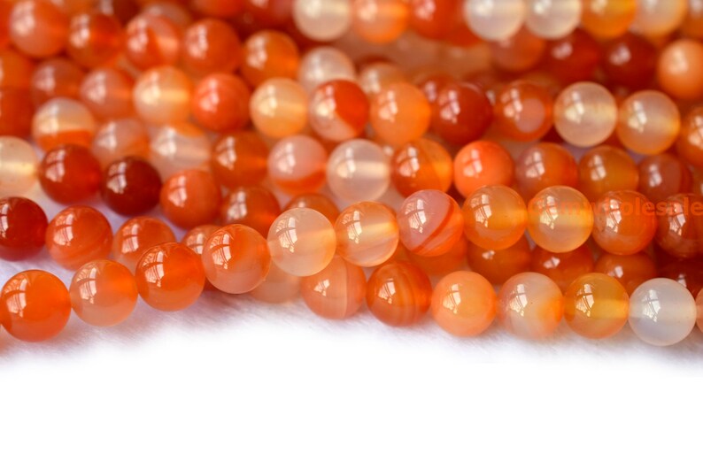 May include: A strand of orange carnelian beads. The beads are round and smooth, with a translucent, agate-like appearance.