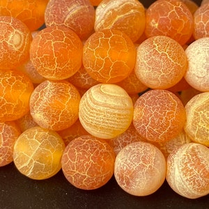 May include: A close-up of a strand of orange agate beads. The beads are round and have a smooth, polished finish. The agate has a natural, cloudy pattern with white and orange swirls.