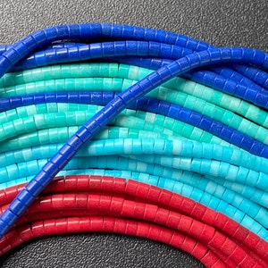 May include: A close-up of a collection of colorful gemstone beads. The beads are arranged in rows, with blue, turquoise, and red beads visible. The beads are all round and have a smooth, polished finish.