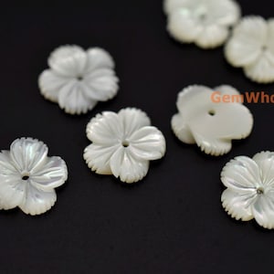 Puede incluir: Cuentas de madreperla blanca con forma de flor con un agujero en el centro. Las cuentas están talladas con detalles intrincados y tienen un brillo nacarado.