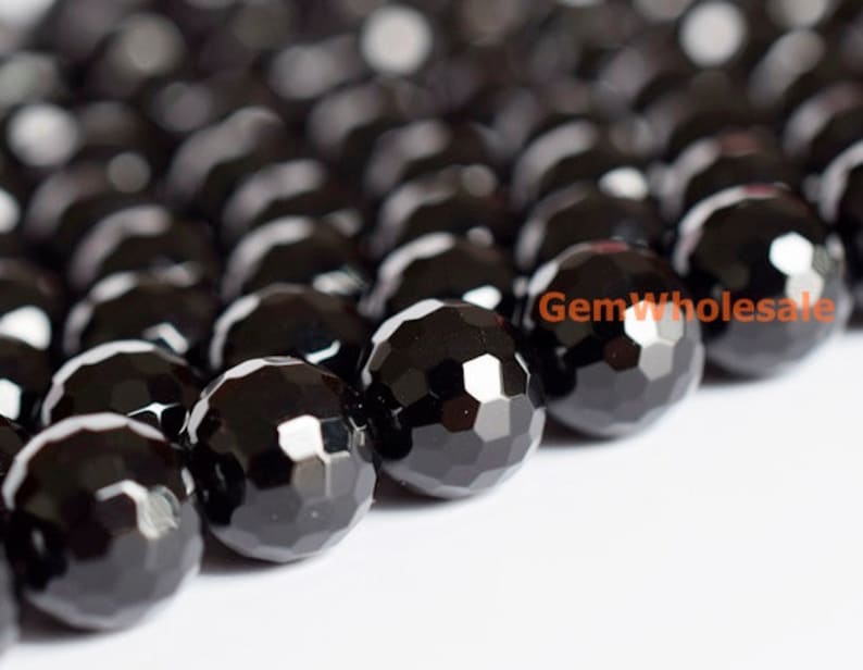 May include: Close-up of a strand of faceted black beads. The beads are round with multiple flat surfaces, creating a sparkling effect. The beads are arranged closely together, suggesting they are strung for jewelry making. The text "GemWholesale" is visible.
