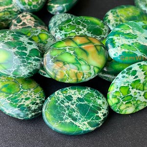 Puede incluir: Primer plano de una colección de cuentas de jaspe ovaladas de color verde y blanco. Las cuentas tienen un patrón de mármol y son lisas y pulidas.