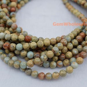 May include: A strand of round, multi-coloured jasper beads. The beads are a mix of brown, beige, and light blue colours. The beads are approximately 6mm in diameter.