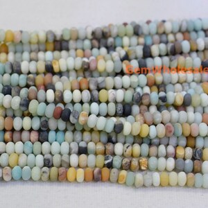 May include: Strands of Amazonite gemstone beads in a variety of colors, including light blue, yellow, brown, and gray. The beads are small, oval-shaped, and strung together, ideal for jewelry making. The beads have a matte finish.