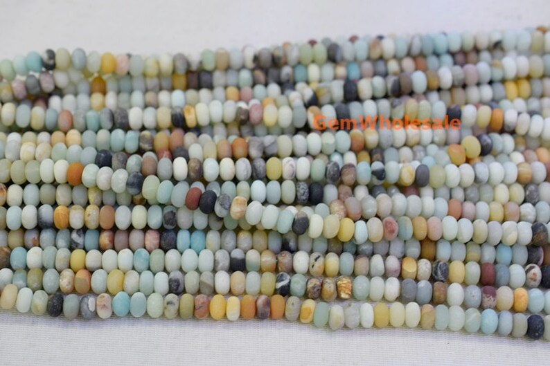 May include: Strands of Amazonite gemstone beads in a variety of colors, including light blue, yellow, brown, and gray. The beads are small, oval-shaped, and strung together, ideal for jewelry making. The beads have a matte finish.