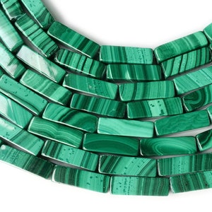 Puede incluir: Una hebra de cuentas de malaquita verde, cada cuenta es un prisma rectangular con una superficie lisa y pulida. Las cuentas están dispuestas en un patrón curvo, mostrando las vetas naturales verdes y blancas de la piedra.
