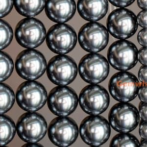 Peut inclure: Un brin de perles grises foncées. Les perles sont rondes et lisses, avec une finition brillante. Les perles sont disposées en rangées, les plus grosses en haut et les plus petites en bas.