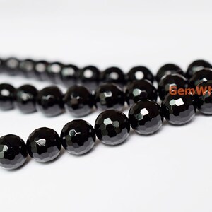 May include: Close-up of a strand of faceted black onyx beads. The beads are round with multiple flat surfaces, creating a sparkling effect. The beads are strung together, and the background is white.