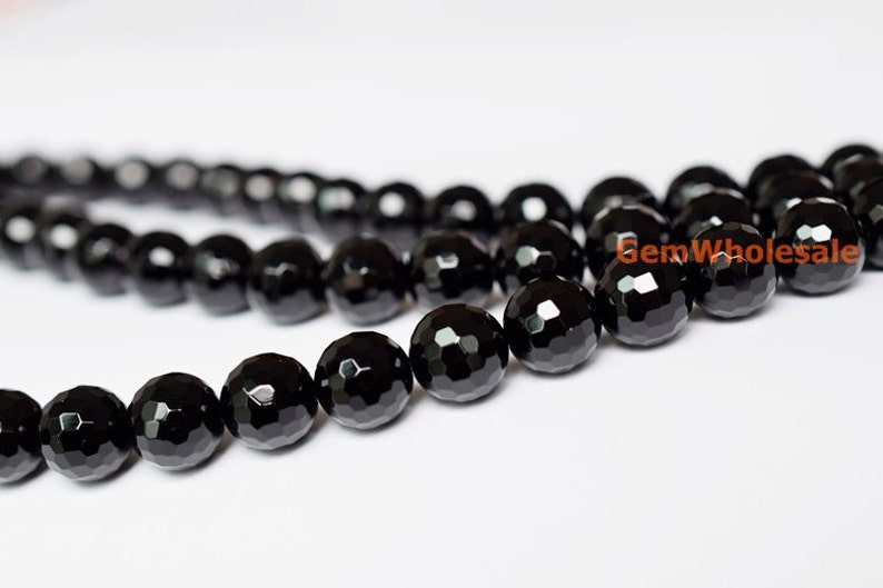 May include: Close-up of a strand of faceted black onyx beads. The beads are round with multiple flat surfaces, creating a sparkling effect. The beads are strung together, and the background is white.