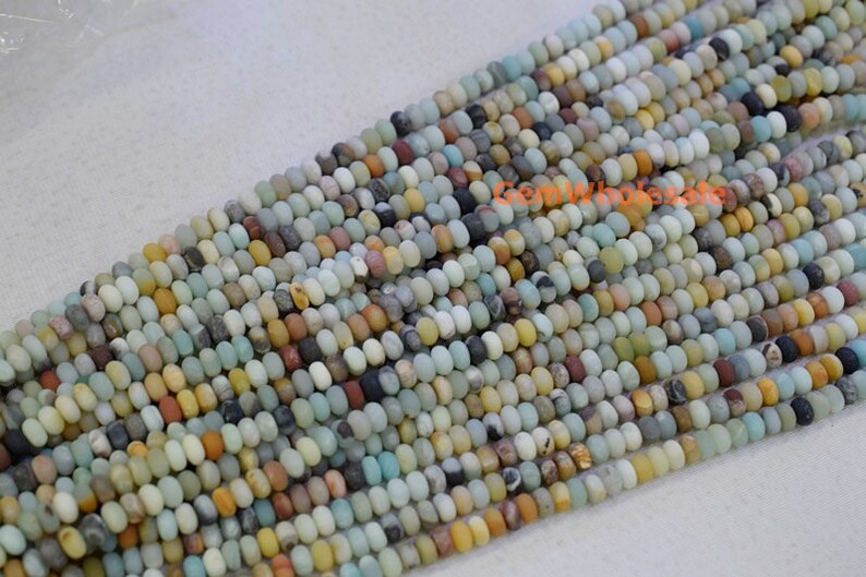 May include: Strands of small, round beads in a variety of colors including beige, brown, gray, and blue-green. The beads are strung together, creating a textured surface. The beads appear to be made of stone or a similar material.