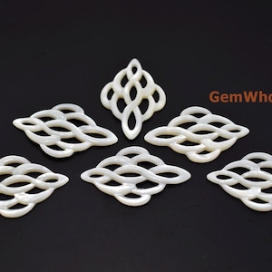 May include: Six white mother of pearl shell pendants with a decorative knot design. The pendants are arranged in a starburst pattern on a black background.