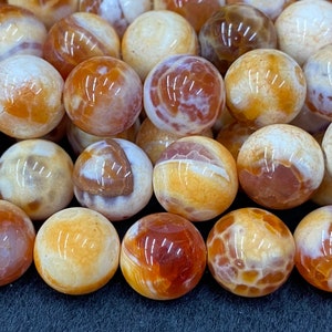 May include: Close-up of a collection of round beads. The beads are a mix of colors, including white, brown, and orange. The beads have a glossy finish and are arranged closely together. The beads are likely used for jewelry making or other crafts.