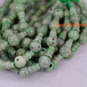 Könnte beinhalten: Eine Strähne grüner Jadeperlen mit einem einzigartigen Design. Jede Perle ist eine runde Kugel mit einer kleineren, zylindrischen Perle, die daran befestigt ist. Die Perlen sind mit einem dünnen, grünen Faden aneinandergereiht.