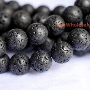 Può includere: Una collana di perline di roccia lavica nera. Le perline sono rotonde e hanno una texture ruvida e porosa.