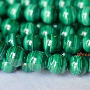 May include: A strand of round, green malachite beads with a striated pattern. The beads are smooth and polished.