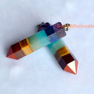 Könnte beinhalten: Zwei sieben Chakra Kristall-Anhänger mit einer silberfarbenen Öse. Die Anhänger bestehen aus geschichteten Steinen in den Farben Rot, Orange, Gelb, Grün, Blau, Indigo und Violett.