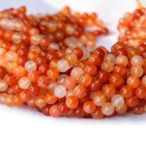 May include: A strand of orange carnelian beads. The beads are round and smooth, with a polished finish. They are a mix of light and dark orange shades.