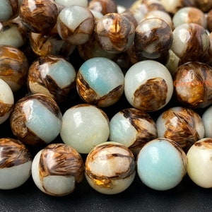 May include: A close-up of a strand of round, light blue and brown agate beads. The beads have a unique, marbled pattern with brown and gold accents.