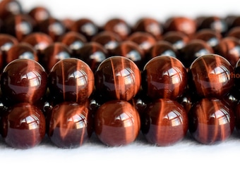 May include: Close-up of a strand of red tiger's eye beads. The beads are round and have a smooth, polished finish. The red tiger's eye stone is known for its chatoyancy, which is the shimmering effect that appears when the stone is turned in the light.